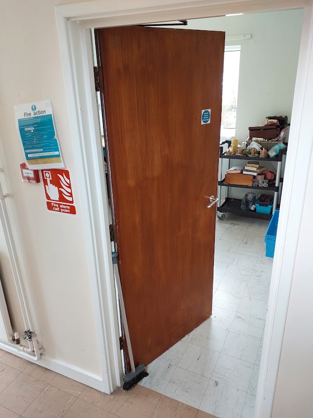 A fire door held open with a wooden wedge on the floor